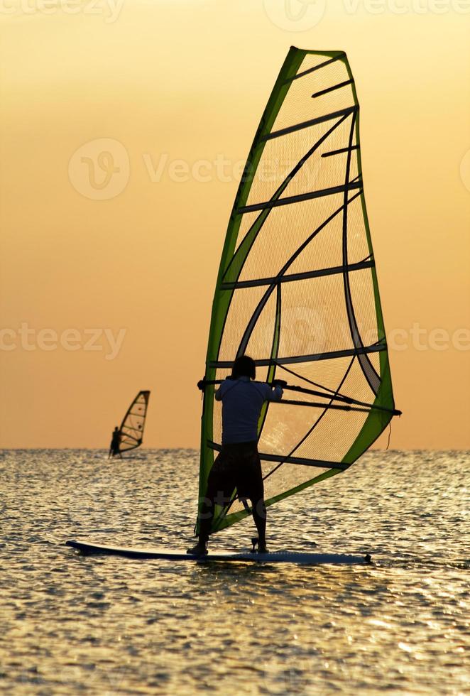 Silhouettes of a windsurfers on waves of a bay photo