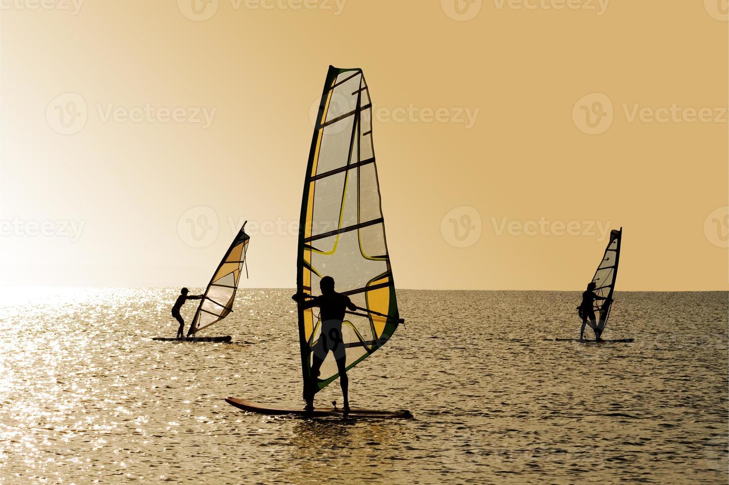 Silhouettes of three windsurfers on waves of a gulf photo