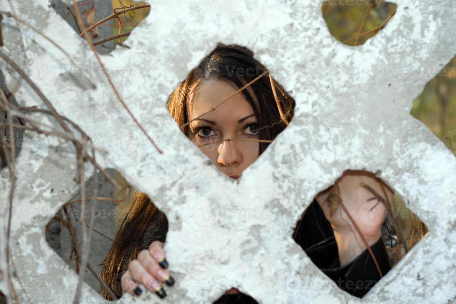 The scared young woman looks through a fence photo