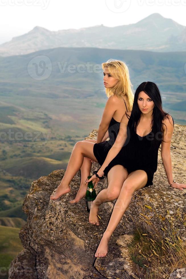 dos mujeres jóvenes con una botella de champán sentadas en una roca foto