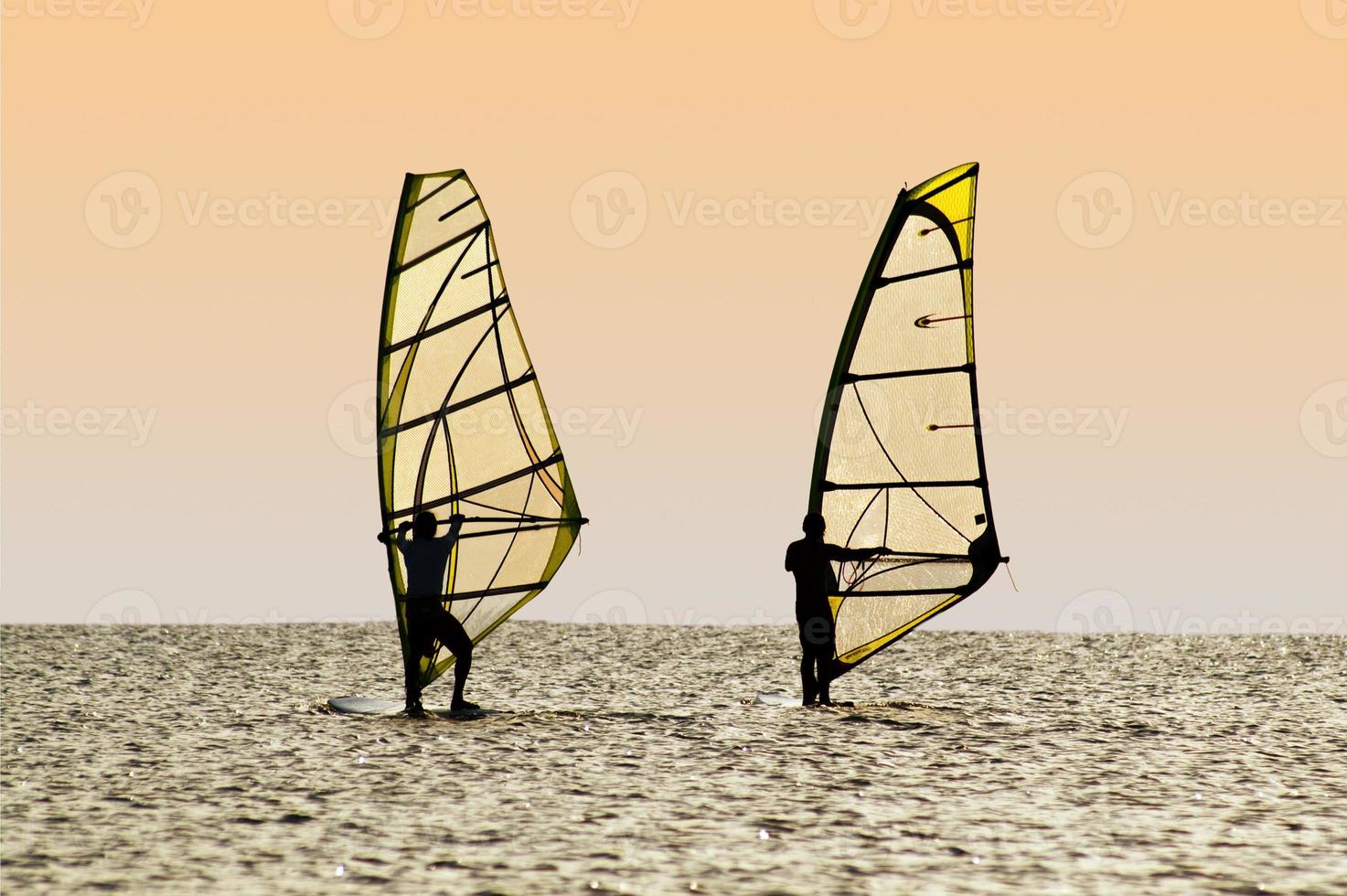 Silhouettes of two windsurfers on waves of a gulf photo