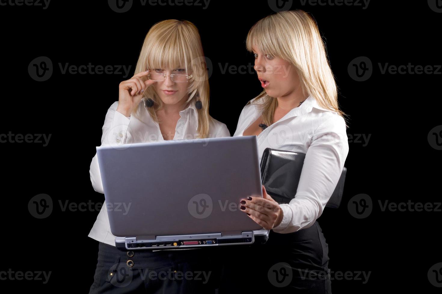 Two young businesswomen with laptop. Isolated on black photo
