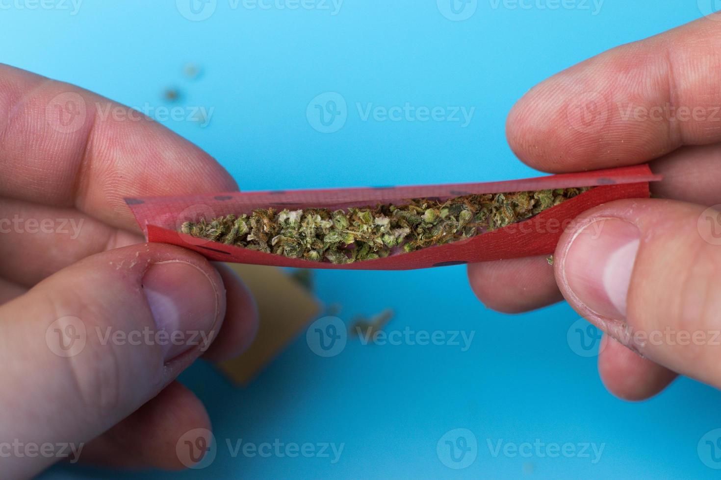 Man rolling joint with fruit tasted paper close-up top view photo