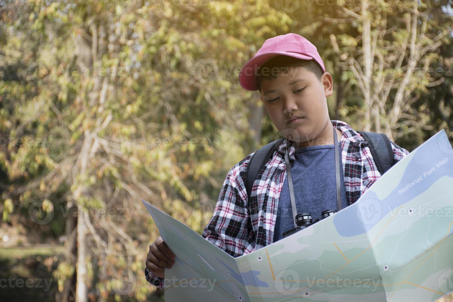 Asian young teen boys hold national park map, reading details of birdwatching before using their binoculars to watch the bird which sitting on brunches and flying in the sky, summer vacation concept. photo