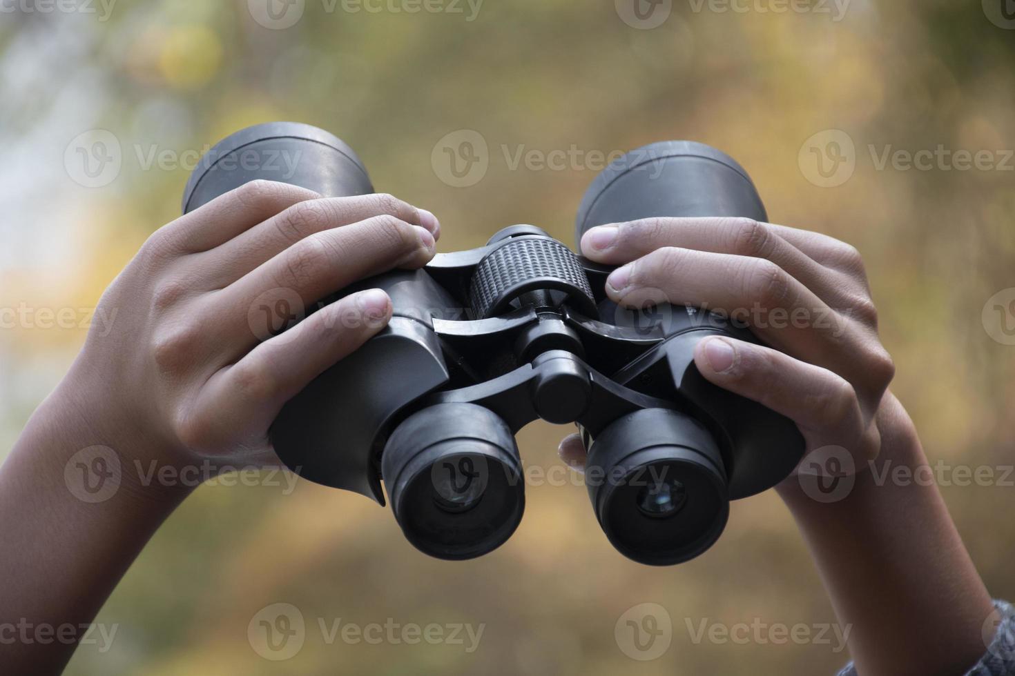 Hands holding binoculars, blurred natural background, concept for vacation, observation, trekking, camping, hiking and birdwatching. photo