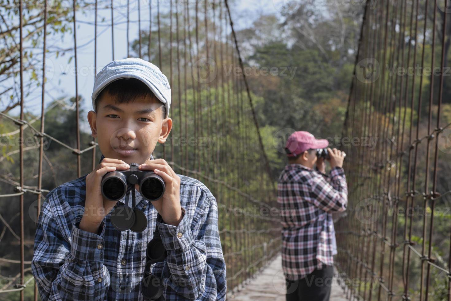Asian boys using binoculars to watch birds on trees and fish in river in local national park during summer camp, idea for learning creatures and wildlife animals and insects outside the classroom. photo