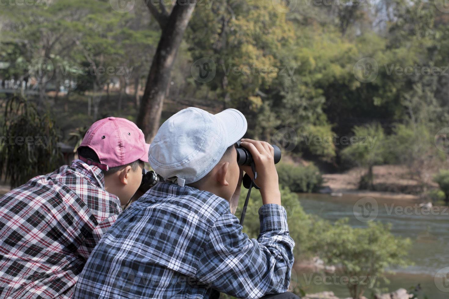 niños asiáticos que usan binoculares para observar pájaros en los árboles y peces en el río en el parque nacional local durante el campamento de verano, idea para aprender criaturas y animales salvajes e insectos fuera del aula. foto