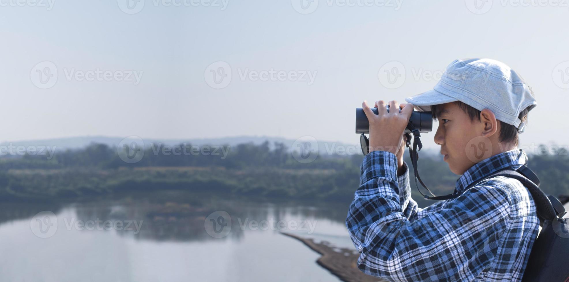 Asian boys using binoculars to watch birds on trees and fish in river in local national park during summer camp, idea for learning creatures and wildlife animals and insects outside the classroom. photo