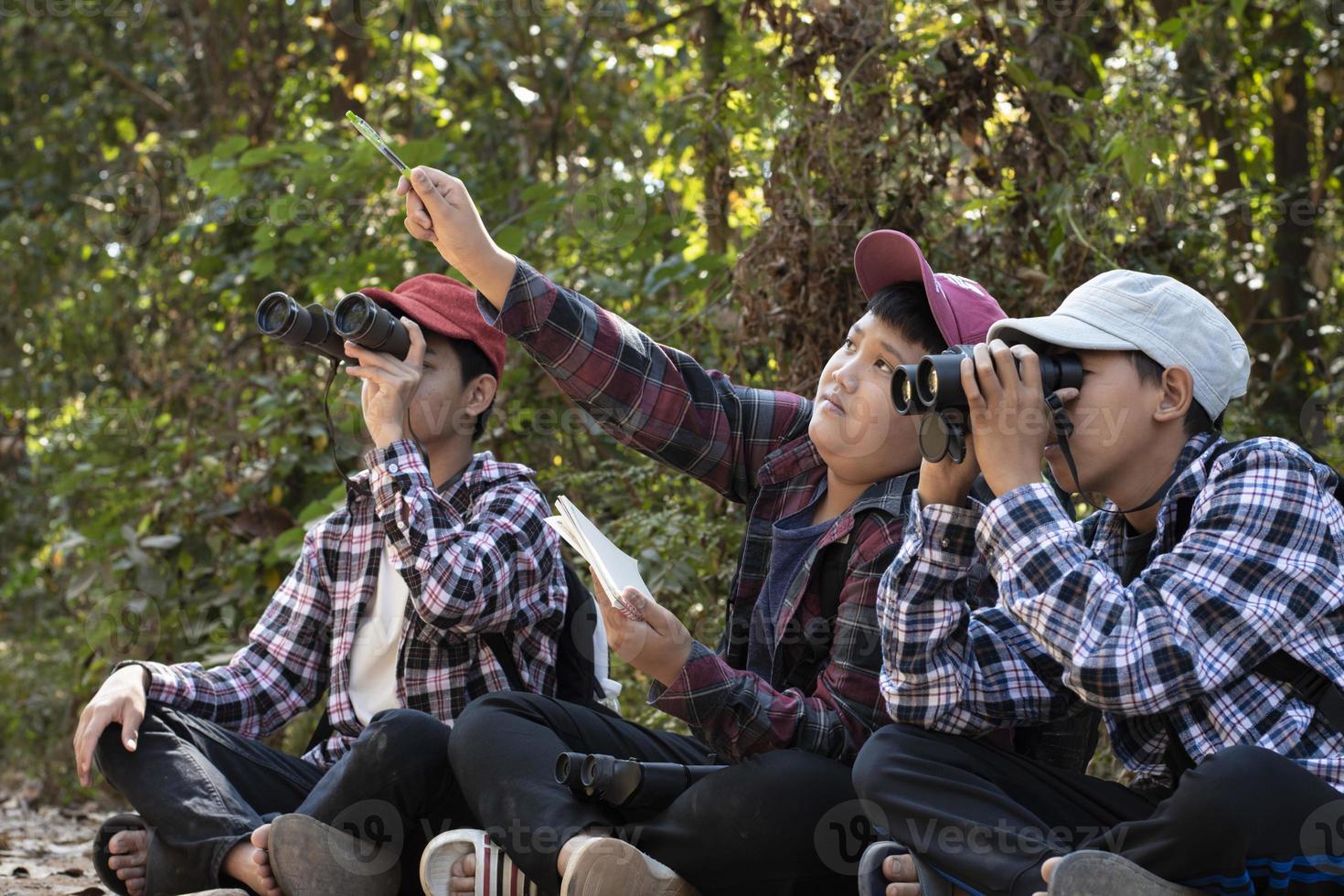 Asian boys using binoculars to watch birds on trees and fish in river in local national park during summer camp, idea for learning creatures and wildlife animals and insects outside the classroom. photo