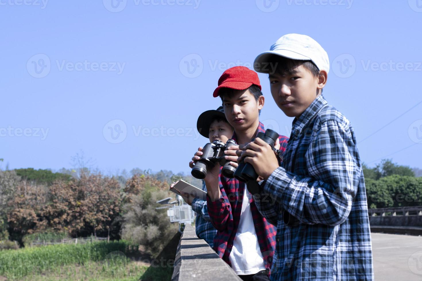 Asian boys using binoculars to watch birds on trees and fish in river in local national park during summer camp, idea for learning creatures and wildlife animals and insects outside the classroom. photo