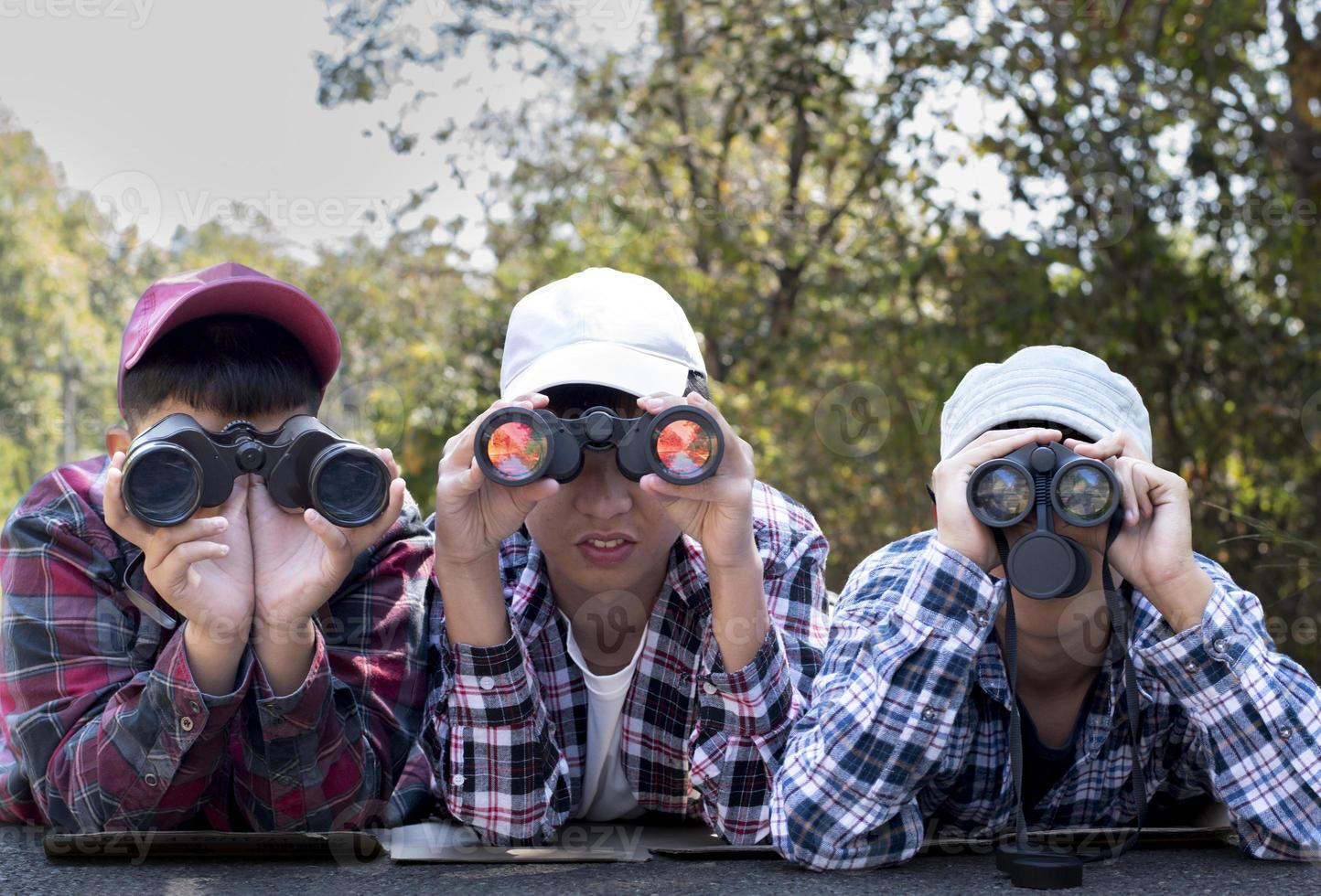 Asian boys using binoculars to watch birds on trees and fish in river in local national park during summer camp, idea for learning creatures and wildlife animals and insects outside the classroom. photo