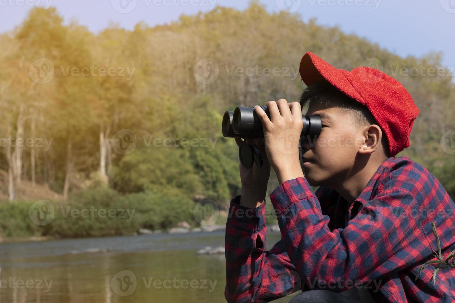 Asian boys using binoculars to watch birds on trees and fish in river in local national park during summer camp, idea for learning creatures and wildlife animals and insects outside the classroom. photo