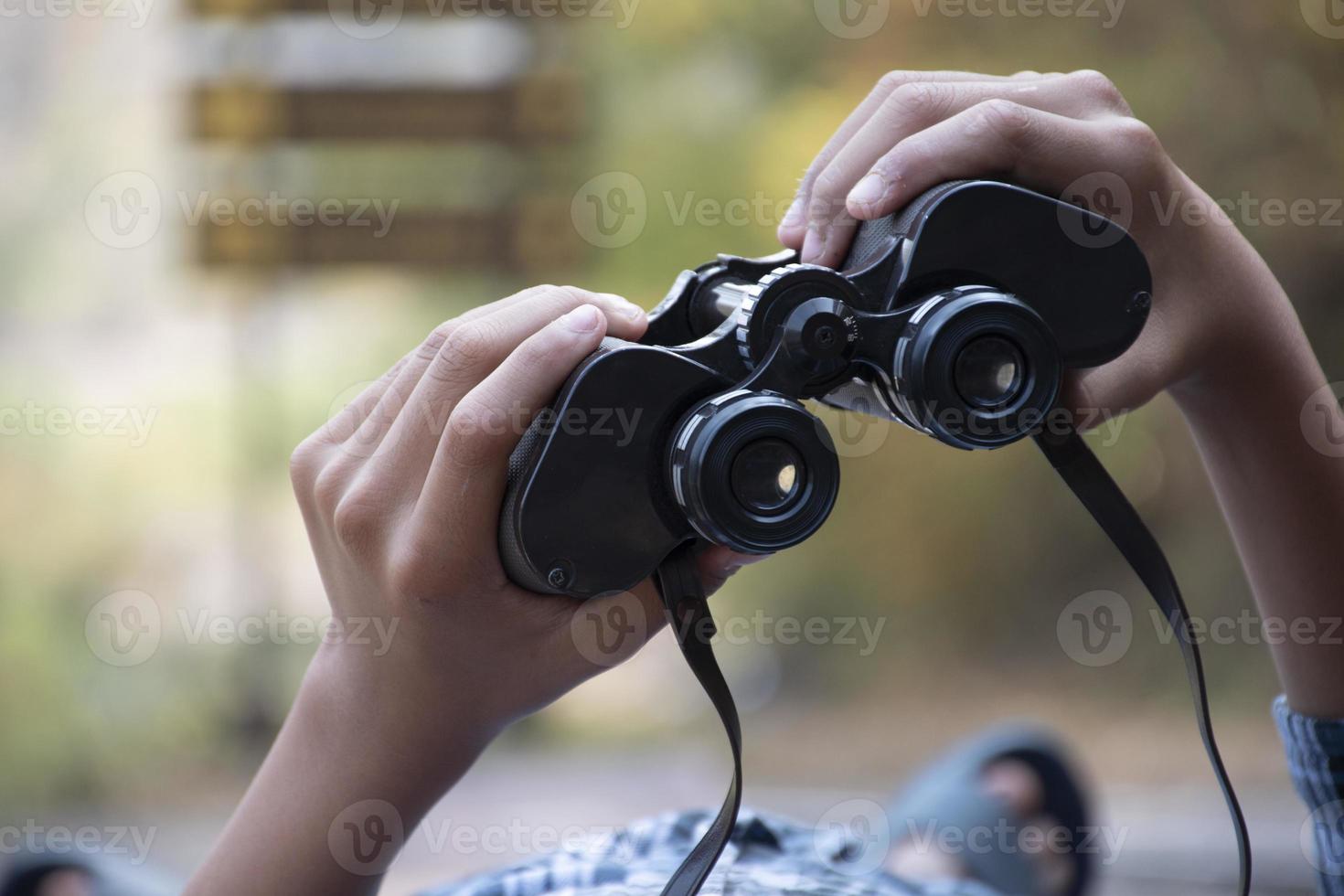 Hands holding binoculars, blurred natural background, concept for vacation, observation, trekking, camping, hiking and birdwatching. photo