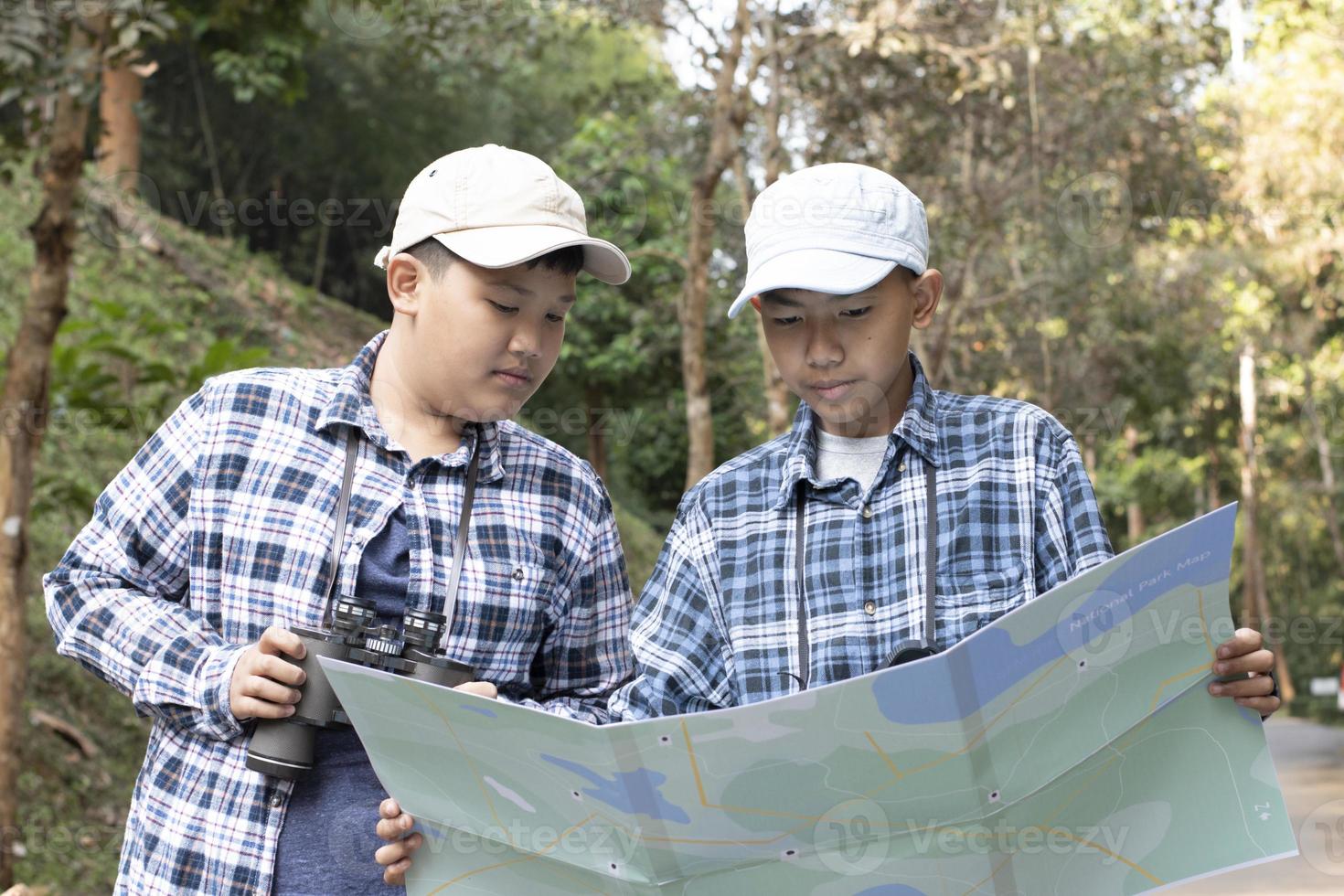 Los jóvenes adolescentes asiáticos sostienen un mapa del parque nacional, leen los detalles de la observación de aves antes de usar sus binoculares para observar al pájaro que se sienta en brunches y vuela en el cielo, concepto de vacaciones de verano. foto