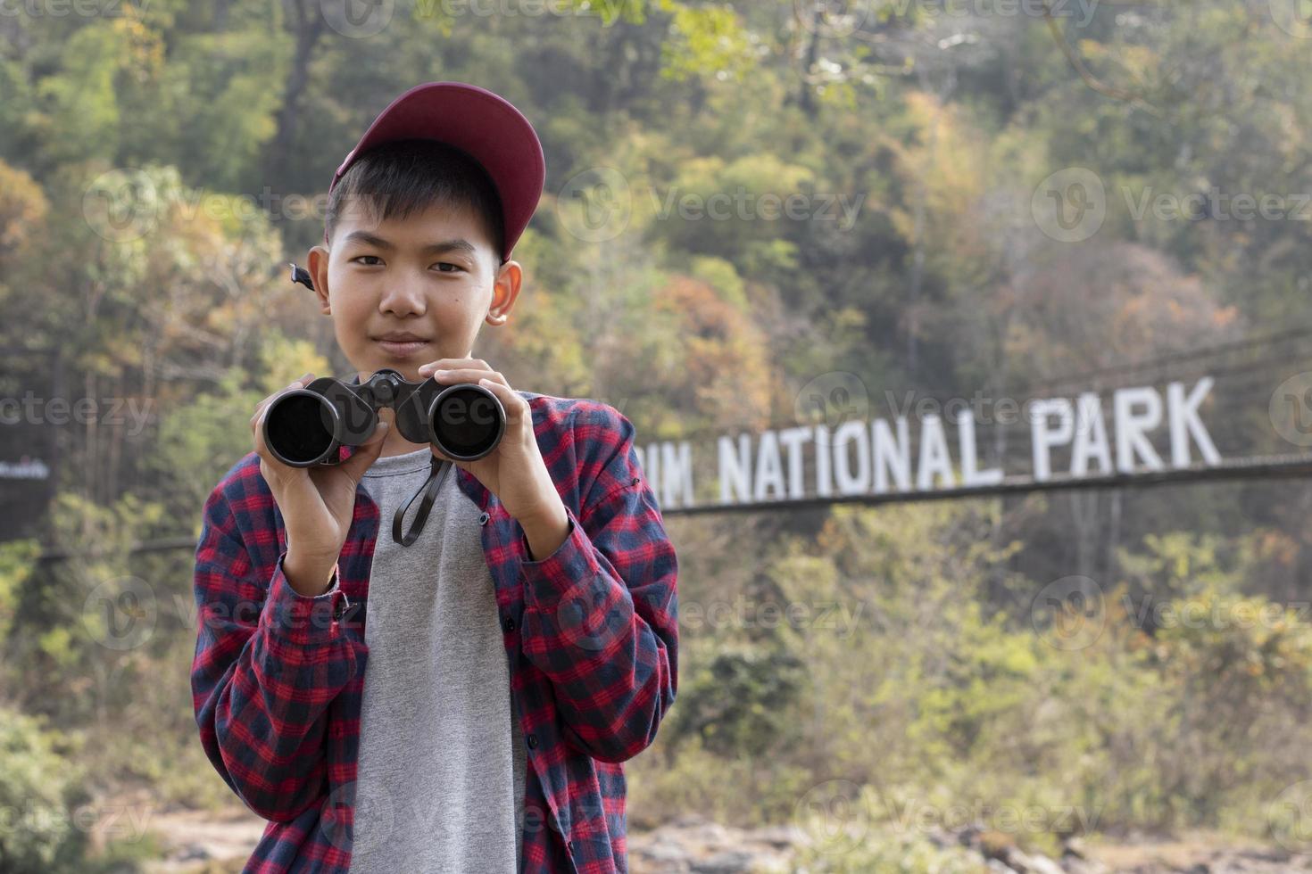 Asian boys using binoculars to watch birds on trees and fish in river in local national park during summer camp, idea for learning creatures and wildlife animals and insects outside the classroom. photo