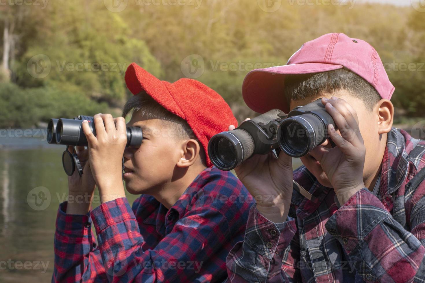 Asian boys are using binoculars to watch birds and fish  in local national park during summer camp, idea for learning creatures and wildlife animals and insects outside the classroom. photo