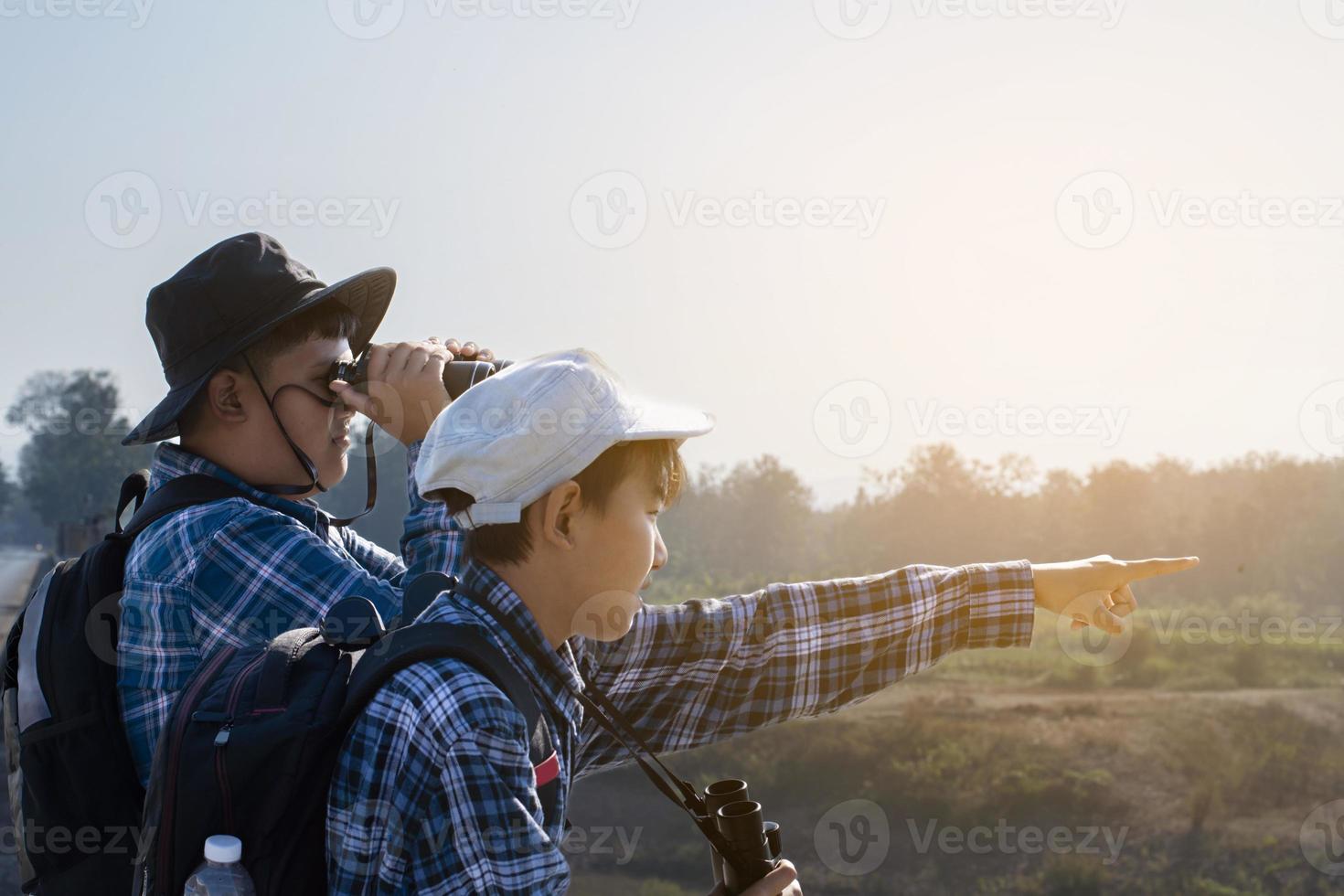 Asian boys using binoculars to watch birds on trees and fish in river in local national park during summer camp, idea for learning creatures and wildlife animals and insects outside the classroom. photo