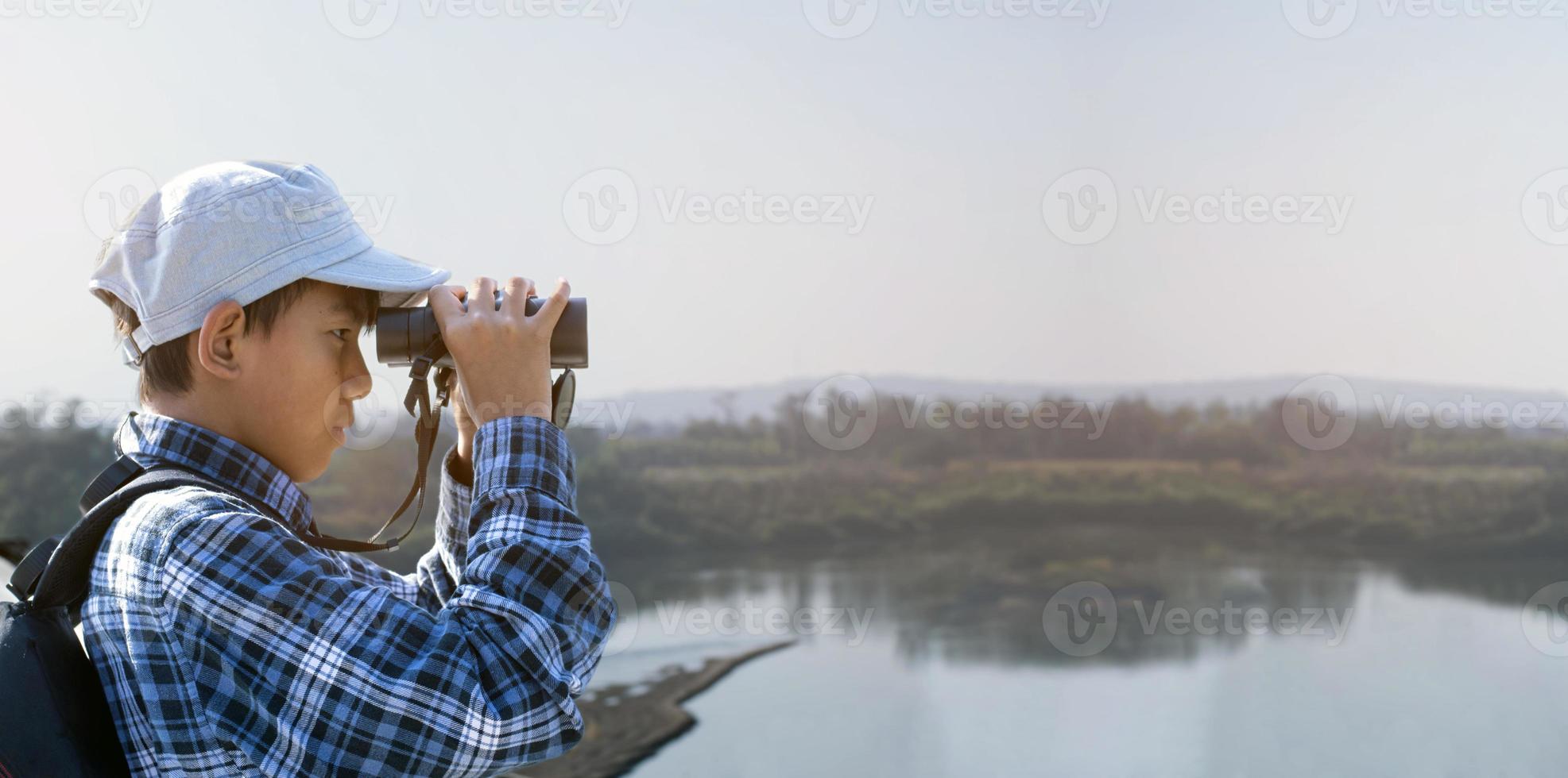 Asian boys using binoculars to watch birds on trees and fish in river in local national park during summer camp, idea for learning creatures and wildlife animals and insects outside the classroom. photo