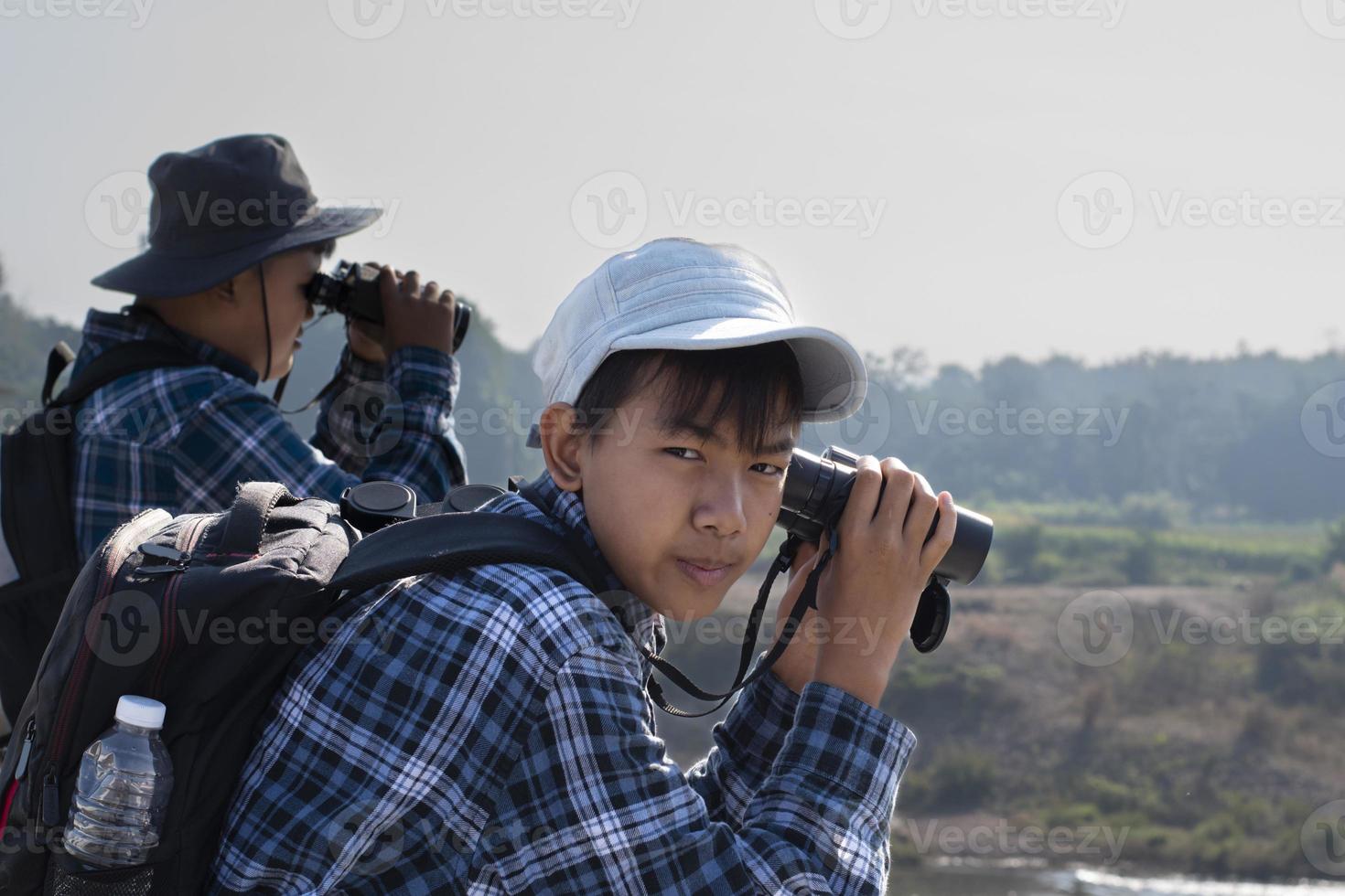 los niños asiáticos están usando binoculares para observar pájaros y peces en el parque nacional local durante el campamento de verano, idea para aprender criaturas y animales salvajes e insectos fuera del aula. foto