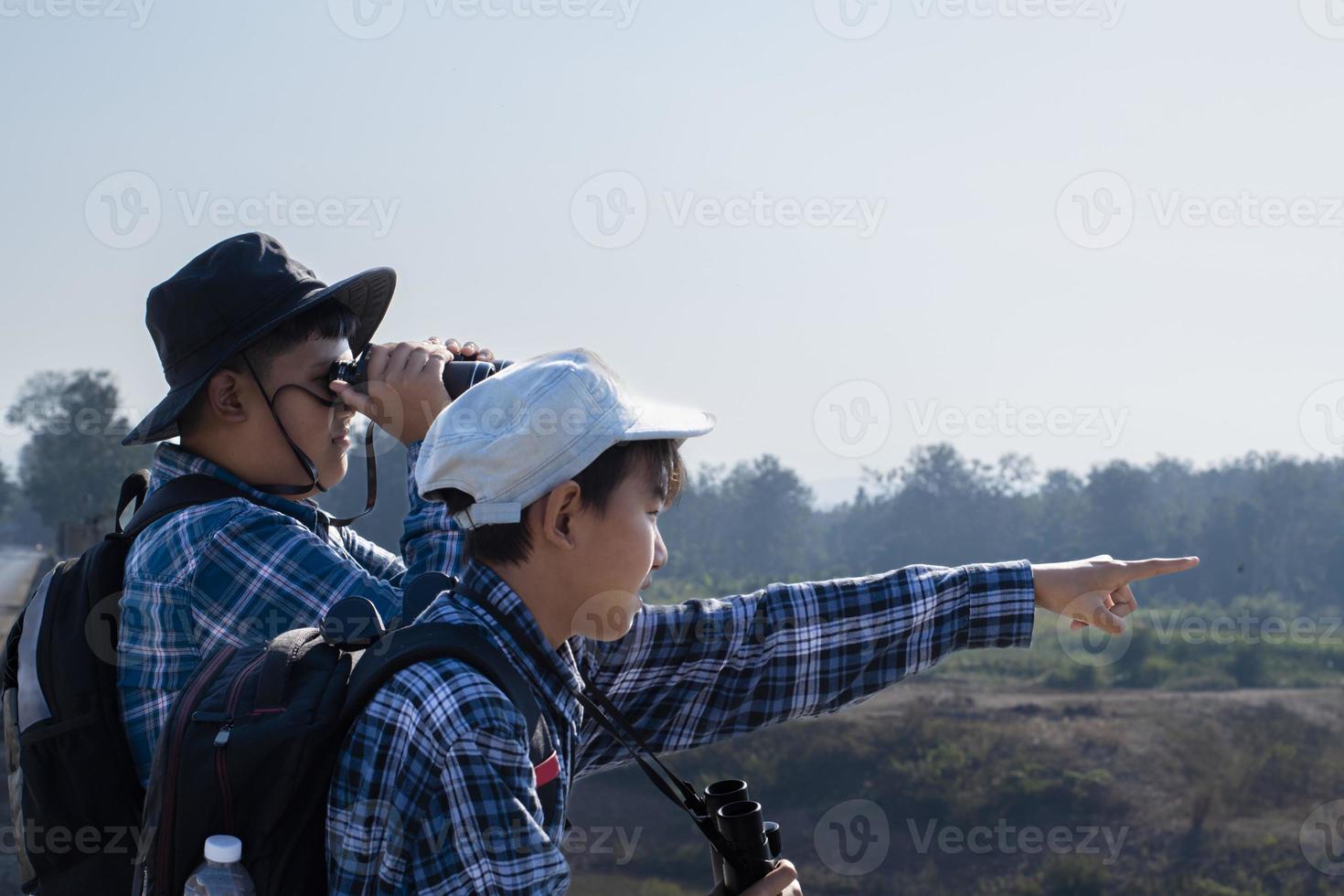 Asian boys using binoculars to watch birds on trees and fish in river in local national park during summer camp, idea for learning creatures and wildlife animals and insects outside the classroom. photo