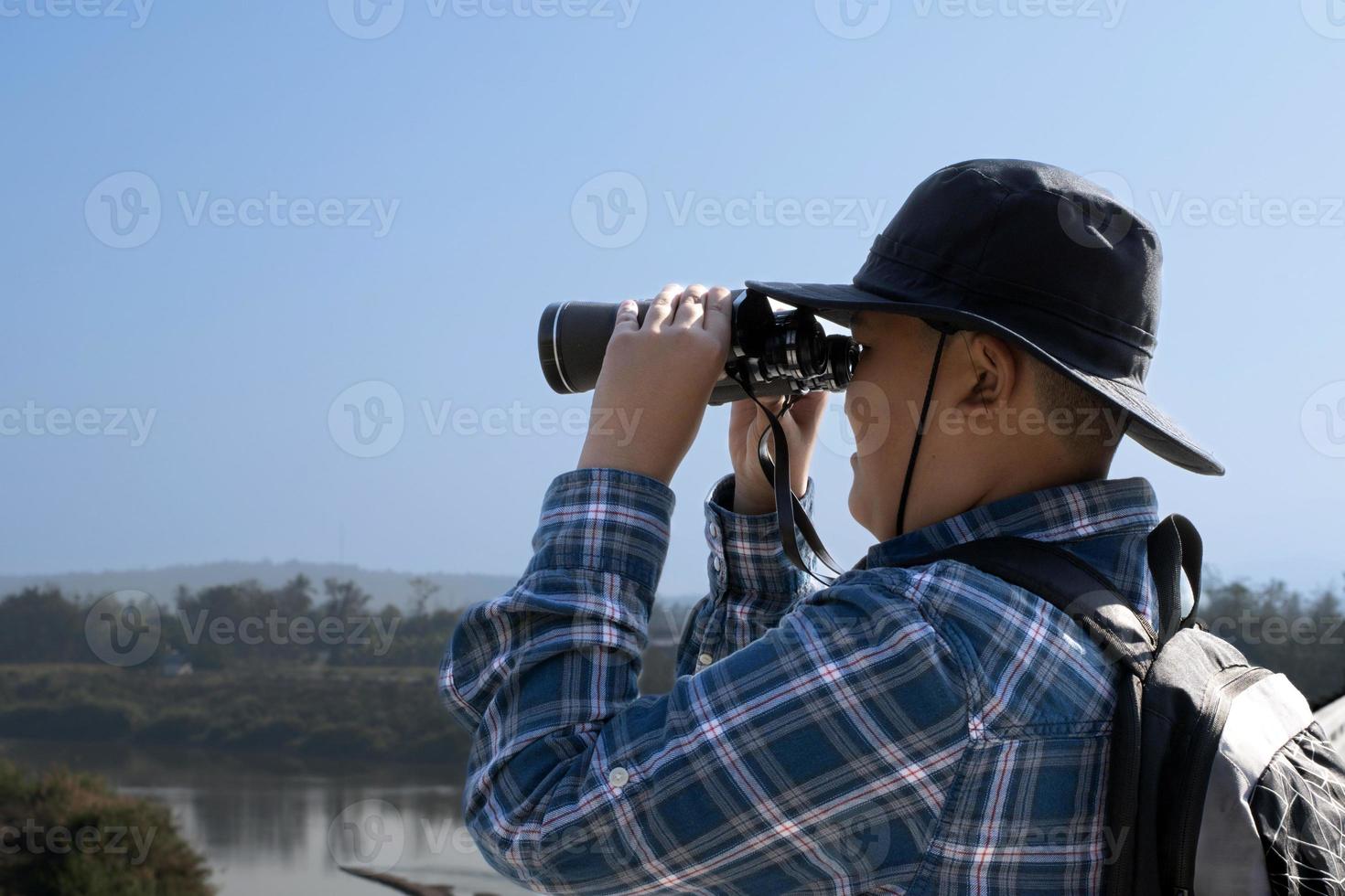 Asian boys using binoculars to watch birds on trees and fish in river in local national park during summer camp, idea for learning creatures and wildlife animals and insects outside the classroom. photo