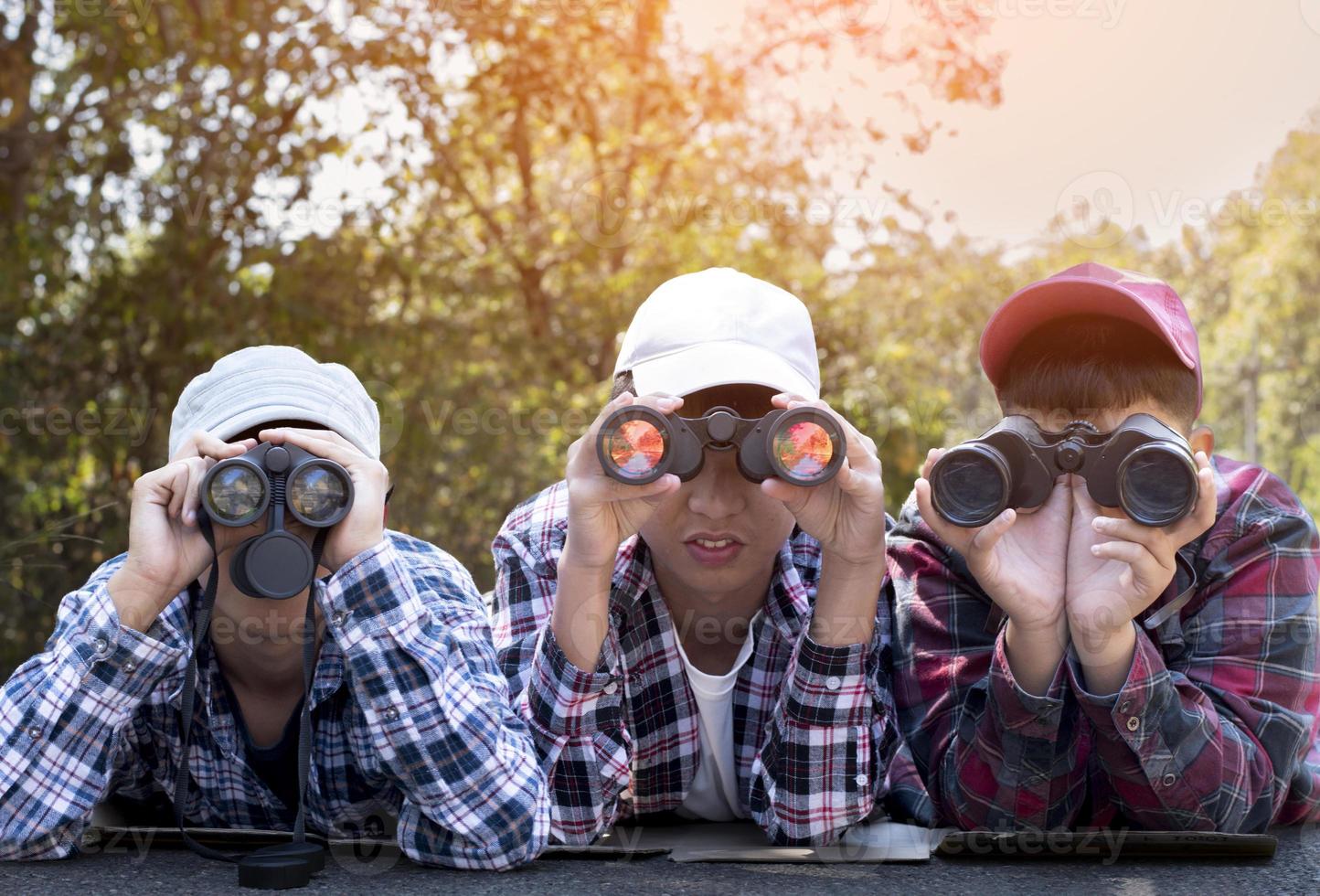 Asian boys using binoculars to watch birds on trees and fish in river in local national park during summer camp, idea for learning creatures and wildlife animals and insects outside the classroom. photo