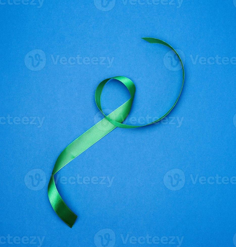 green silk thin ribbon twisted on a blue background photo