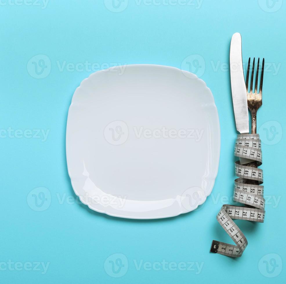 knife with a fork wrapped in a measuring tape with a white ceramic plate photo