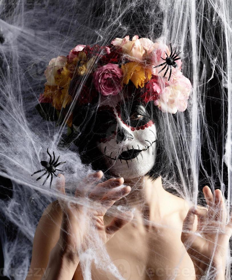 la chica con el pelo negro está vestida con una corona de rosas multicolores y el maquillaje está hecho en su cara calavera de azúcar hasta el día de los muertos foto