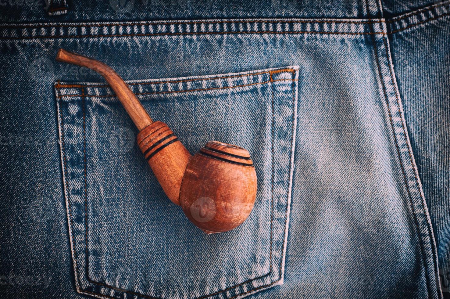 Wooden pipe for tobacco is in the back pocket of old blue jeans photo