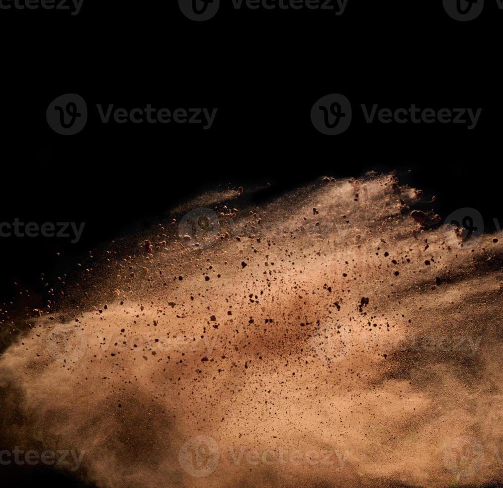 flying brown cocoa particles on a black background. Powder flies up photo