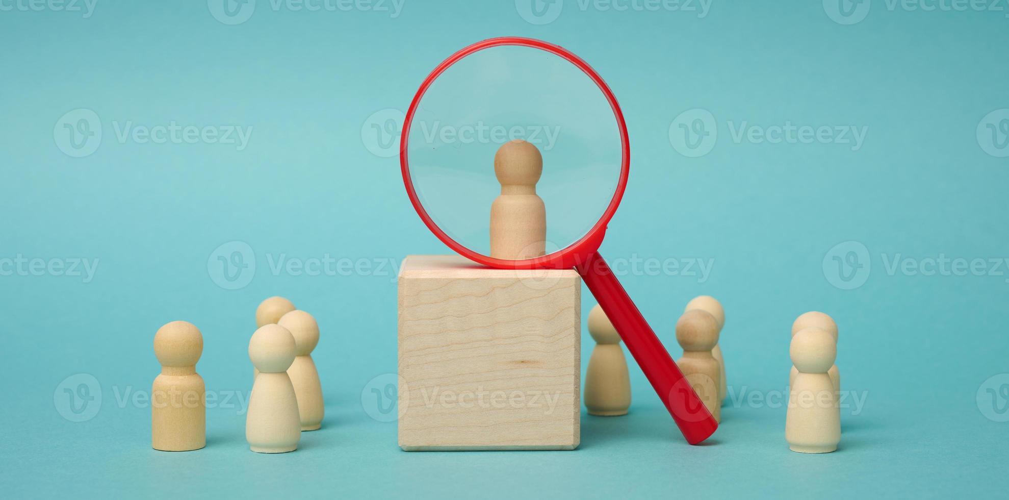 wooden figures of men stand on a beige background and a plastic magnifying glass. Recruitment concept, search for talented and capable employees photo