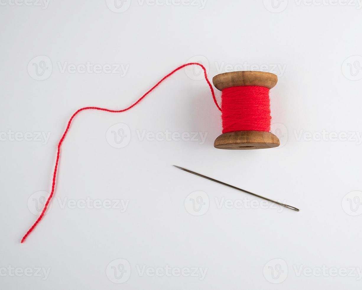 wooden reel with red wool thread and a large needle photo