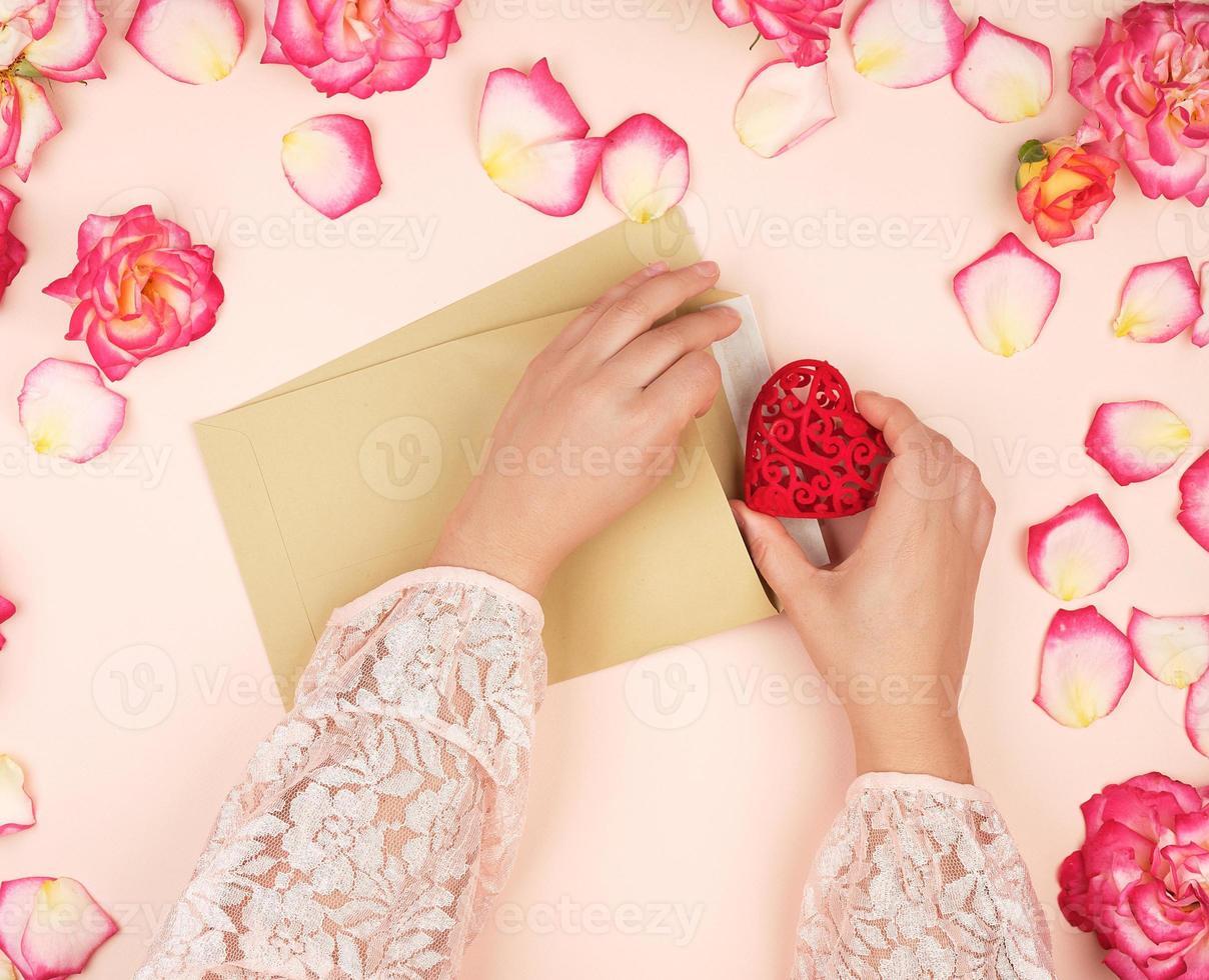two female hands put a red heart in a brown paper envelope photo