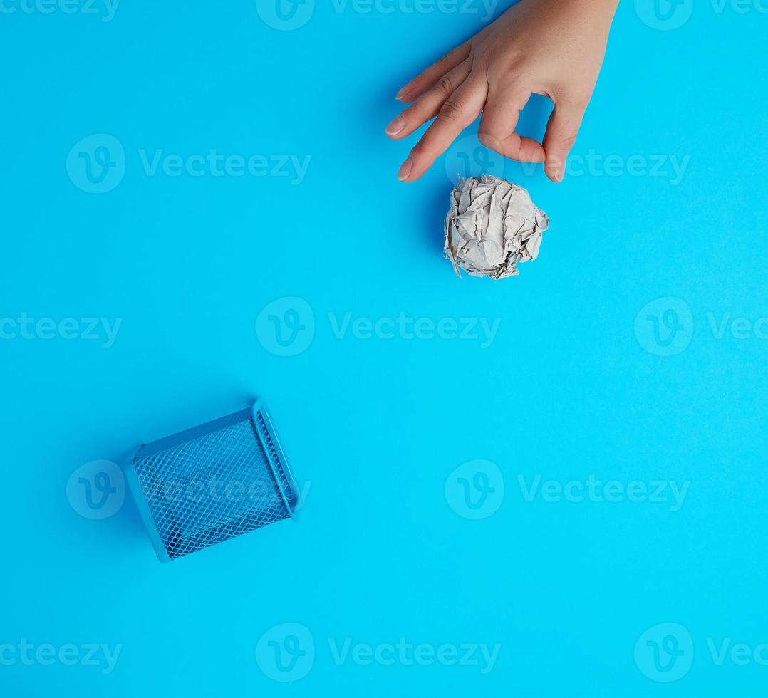hand pushed a ball of crumpled gray paper into a metal wastebasket photo