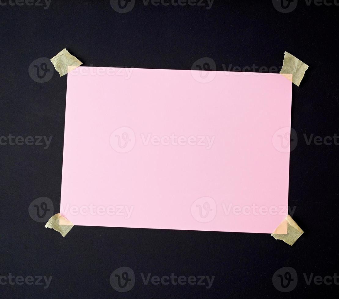A4 blank white sheet attached with adhesive tape to a black wooden surface photo