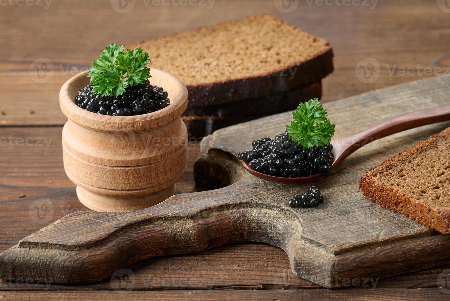 fresh grainy black paddlefish caviar in brown wooden spoon on a brown table, close up photo