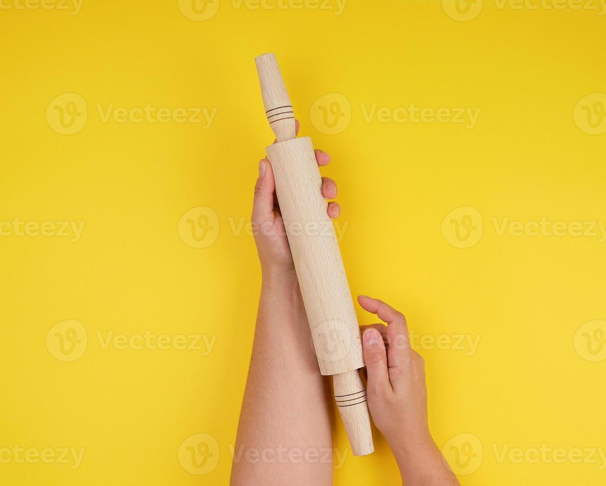hand holding a wooden rolling pin on a yellow background photo