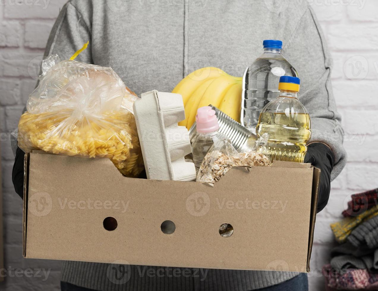 woman in a gray sweater is packing food in a cardboard box, the concept of assistance and volunteering photo
