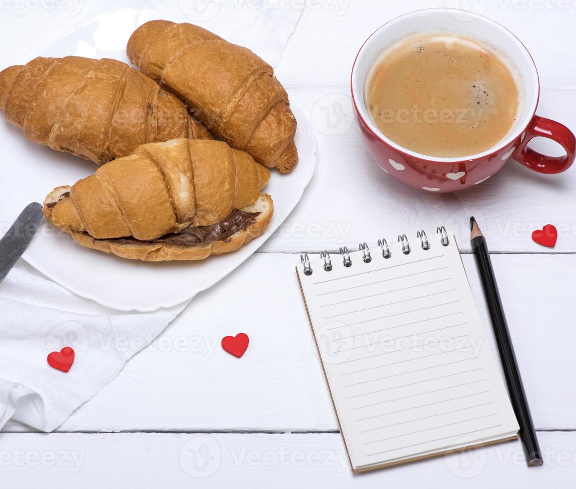 red ceramic mug with hot coffee and fresh croissants photo