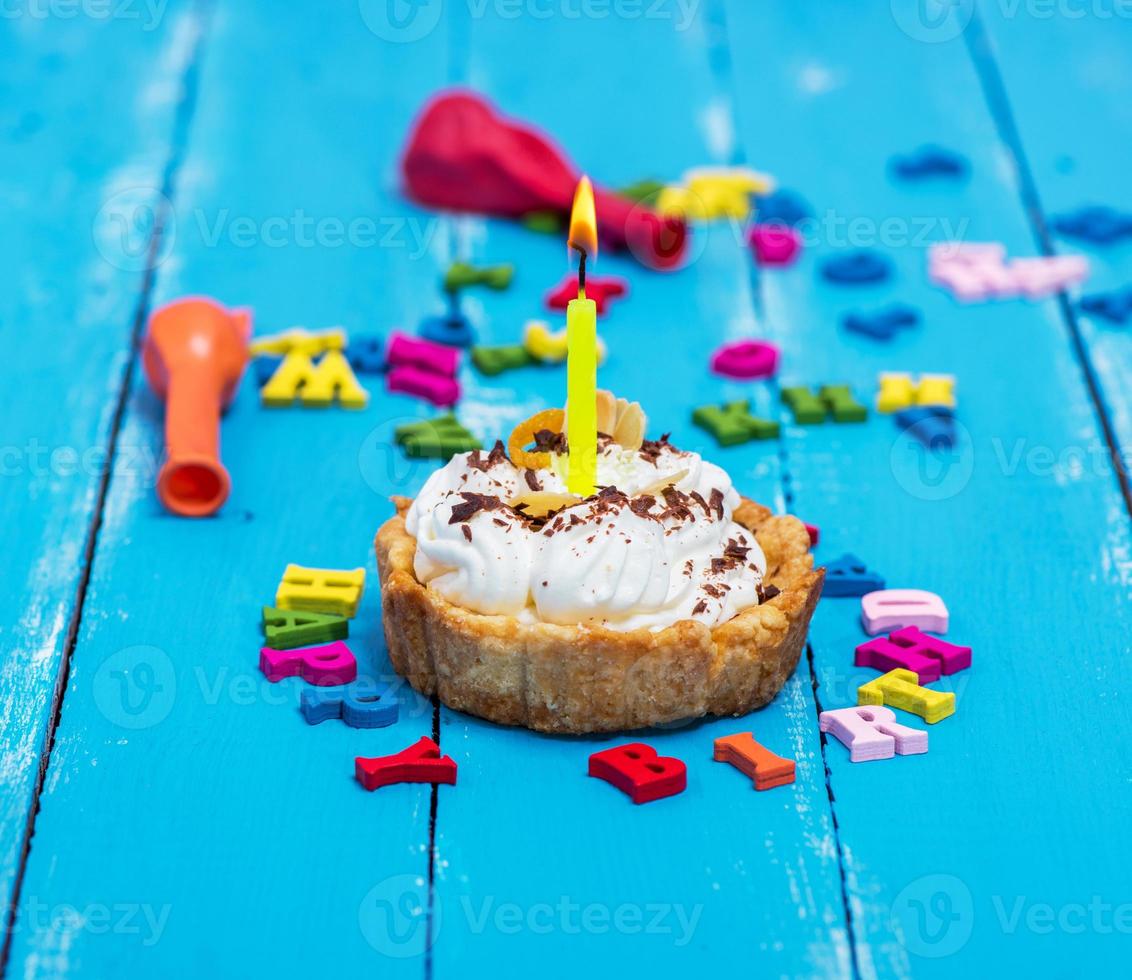 sweet cake with white cream and a burning yellow candle photo