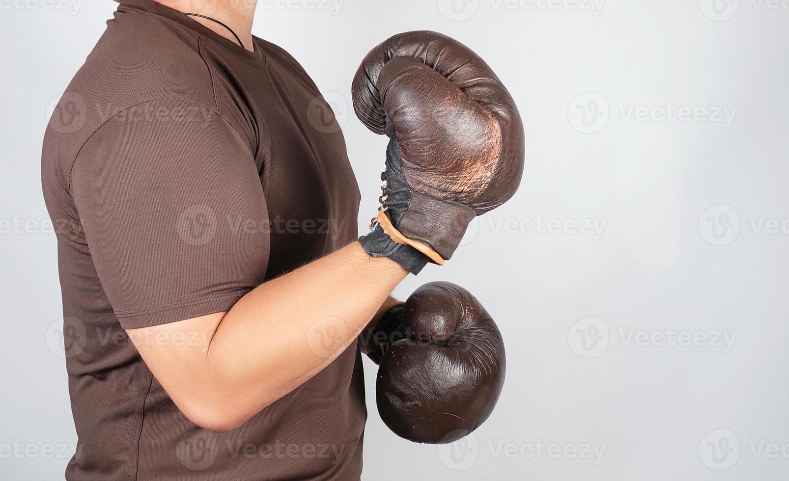 joven parado en un estante de boxeo, usando guantes de boxeo marrones muy viejos en sus manos foto