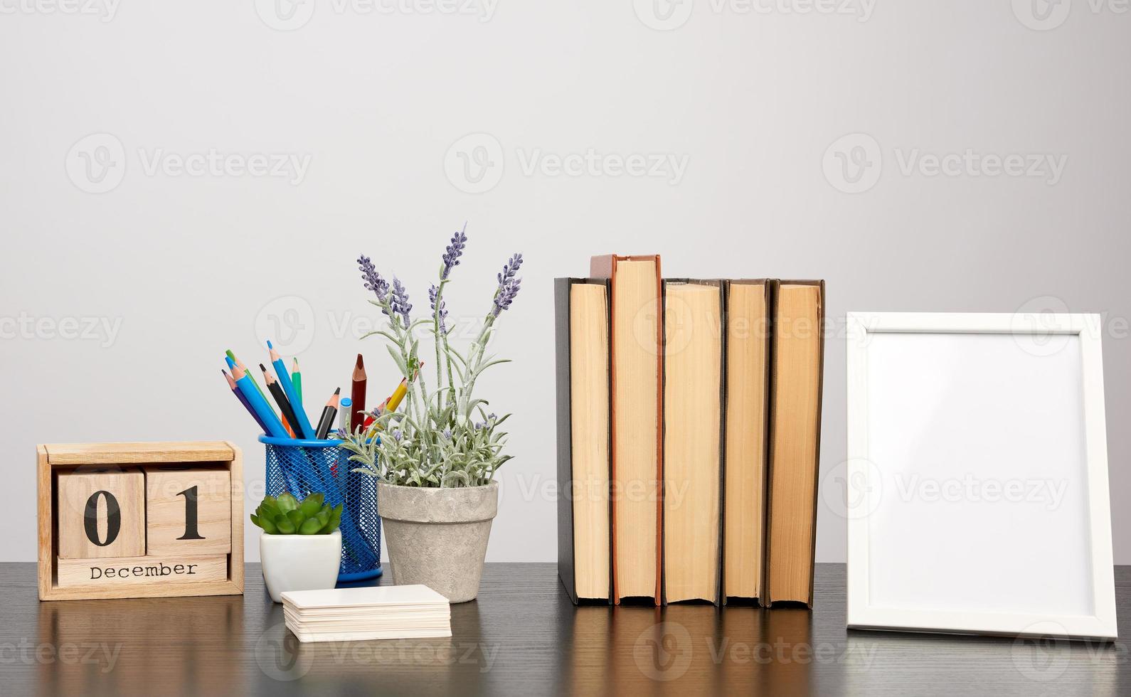 empty white photo frame, stack of books and a pot of growing lavender on a black table