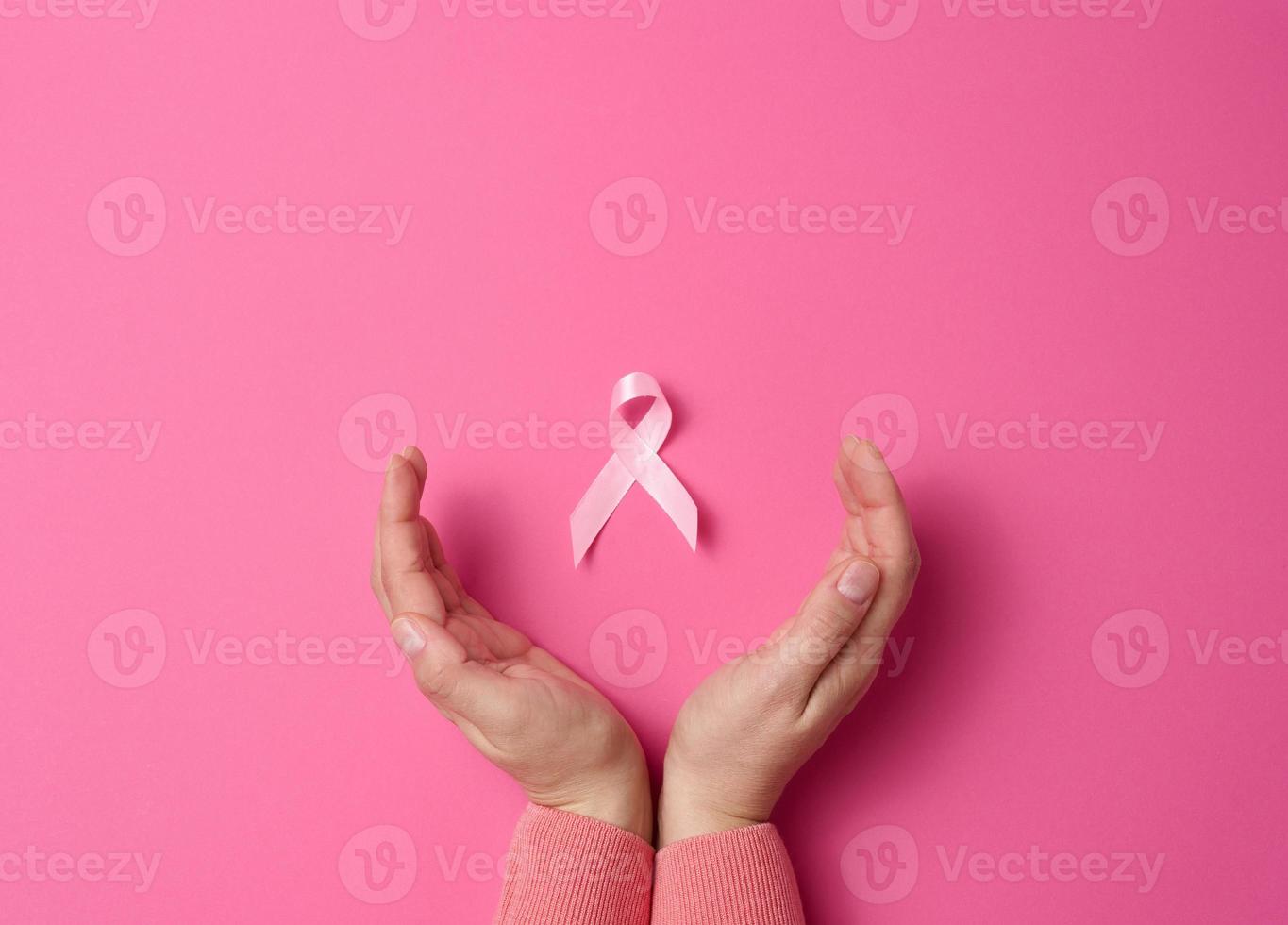 dos manos femeninas sostienen una cinta de seda rosa en forma de bucle sobre un fondo rosa. símbolo de la lucha contra el cáncer de mama foto