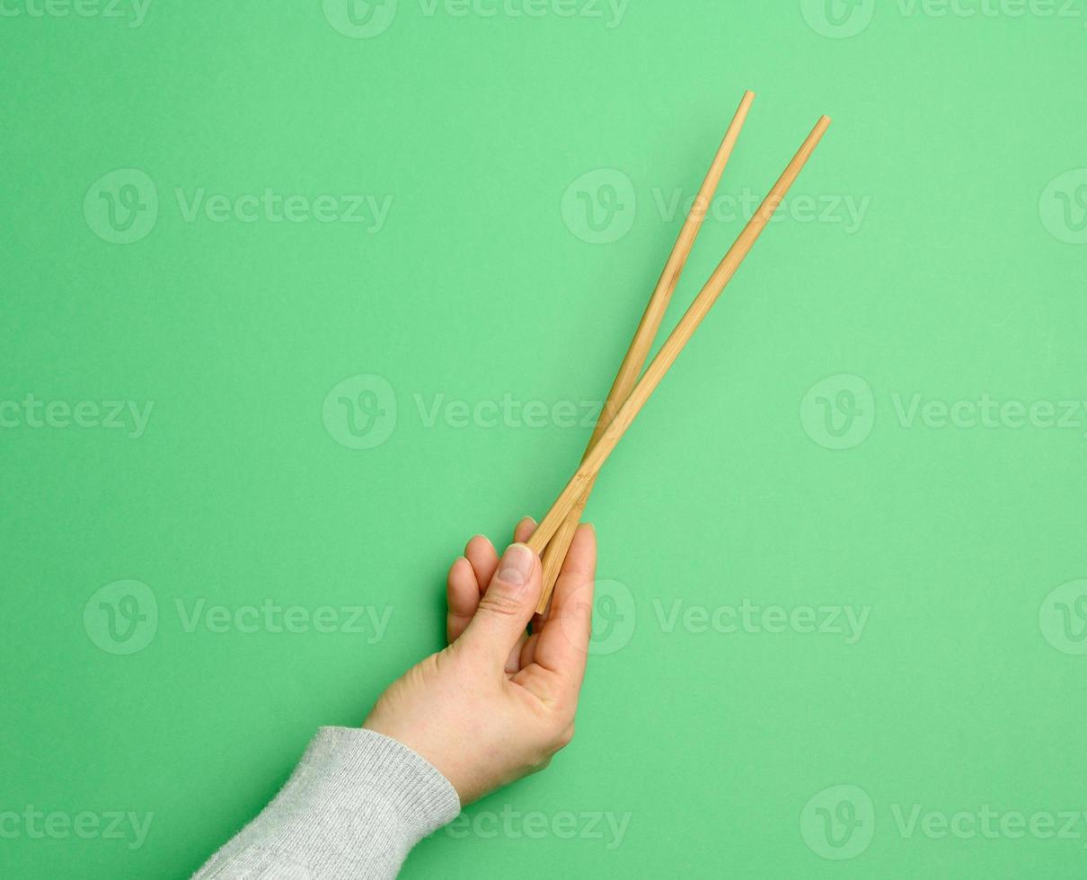 un par de palillos de madera en una mano femenina sobre un fondo verde foto