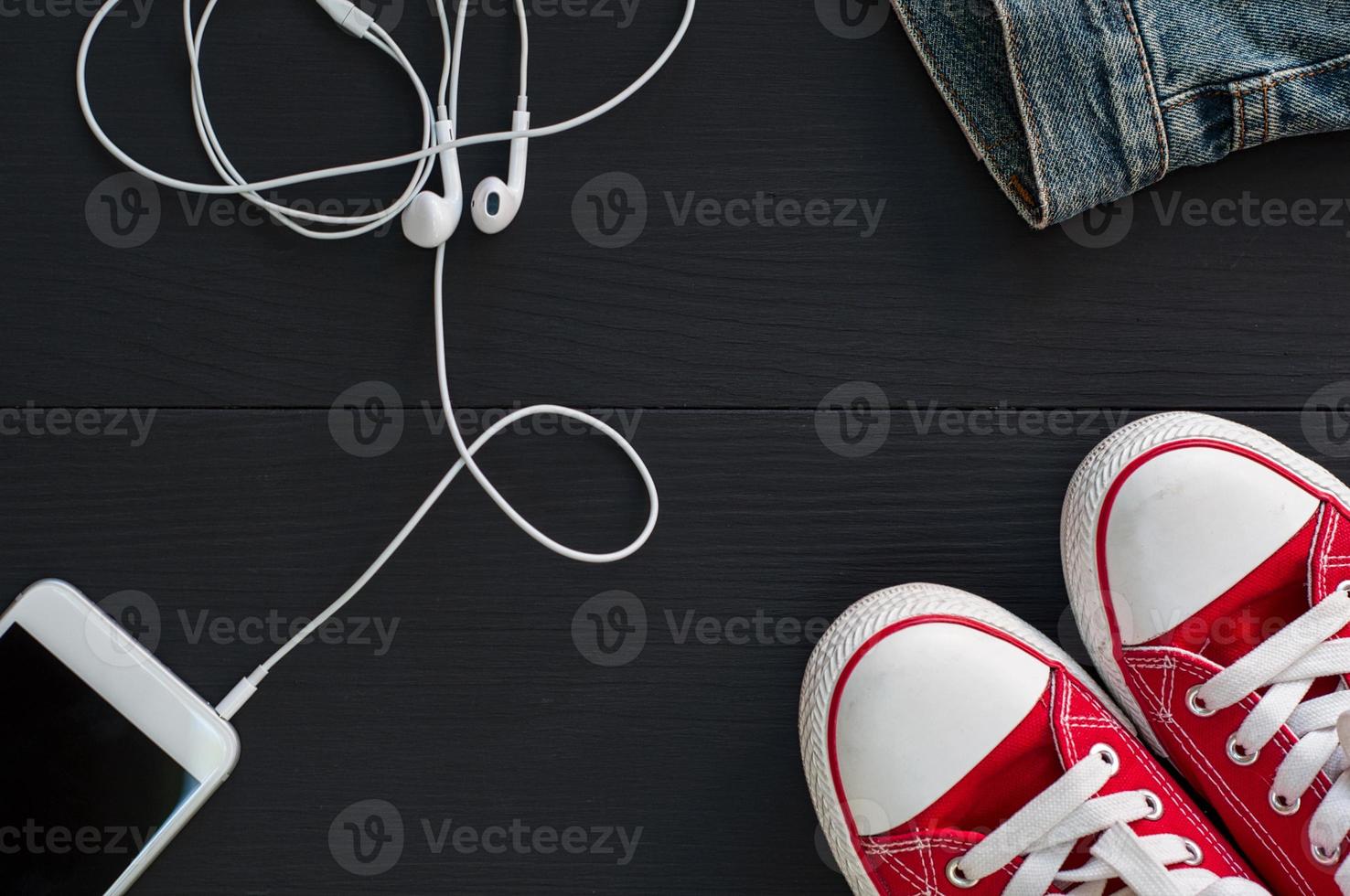 Smartphone with headphones and red sneakers on a black wooden surface photo