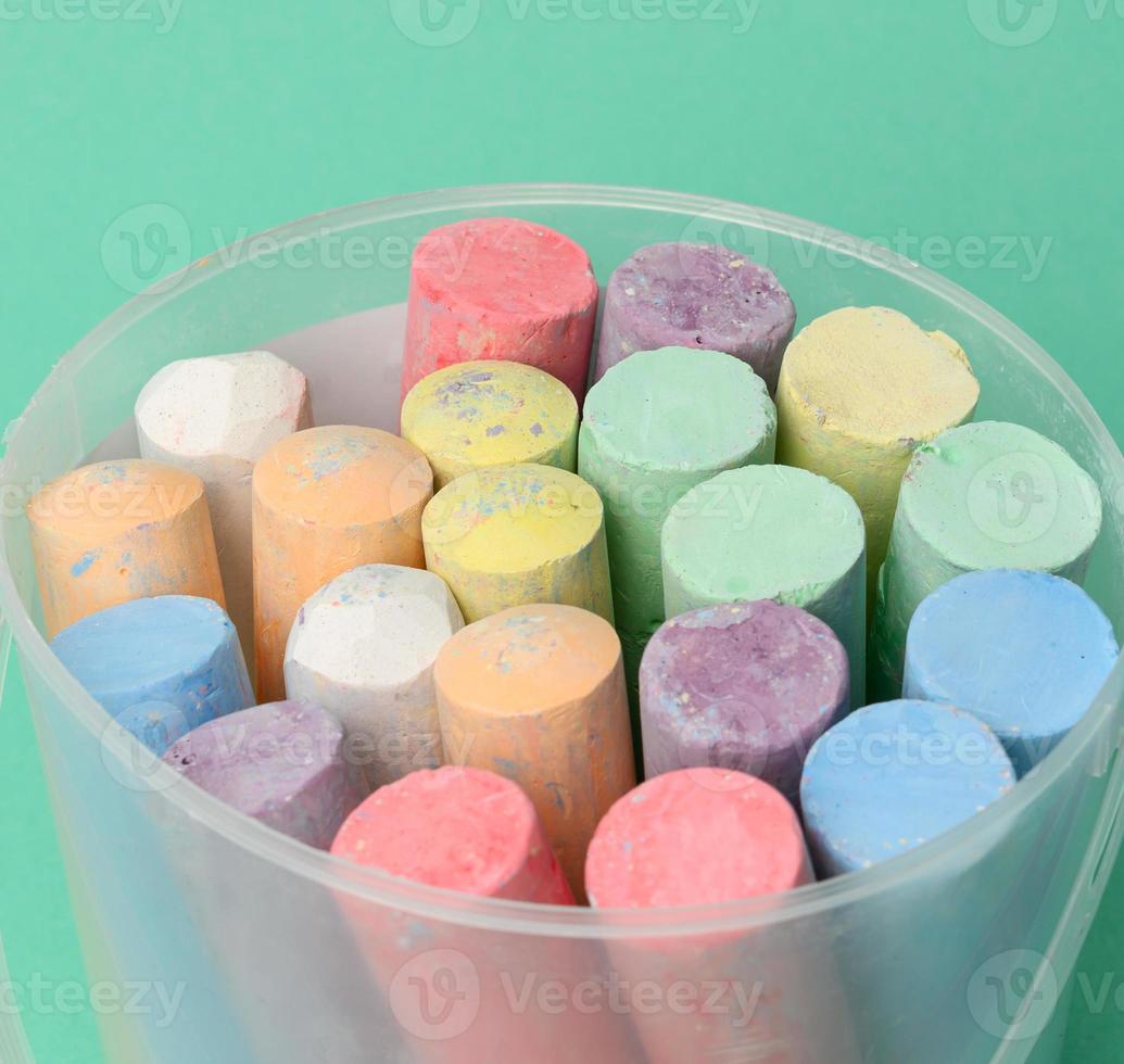 multicolored chalk in a plastic bucket on a green background, photo