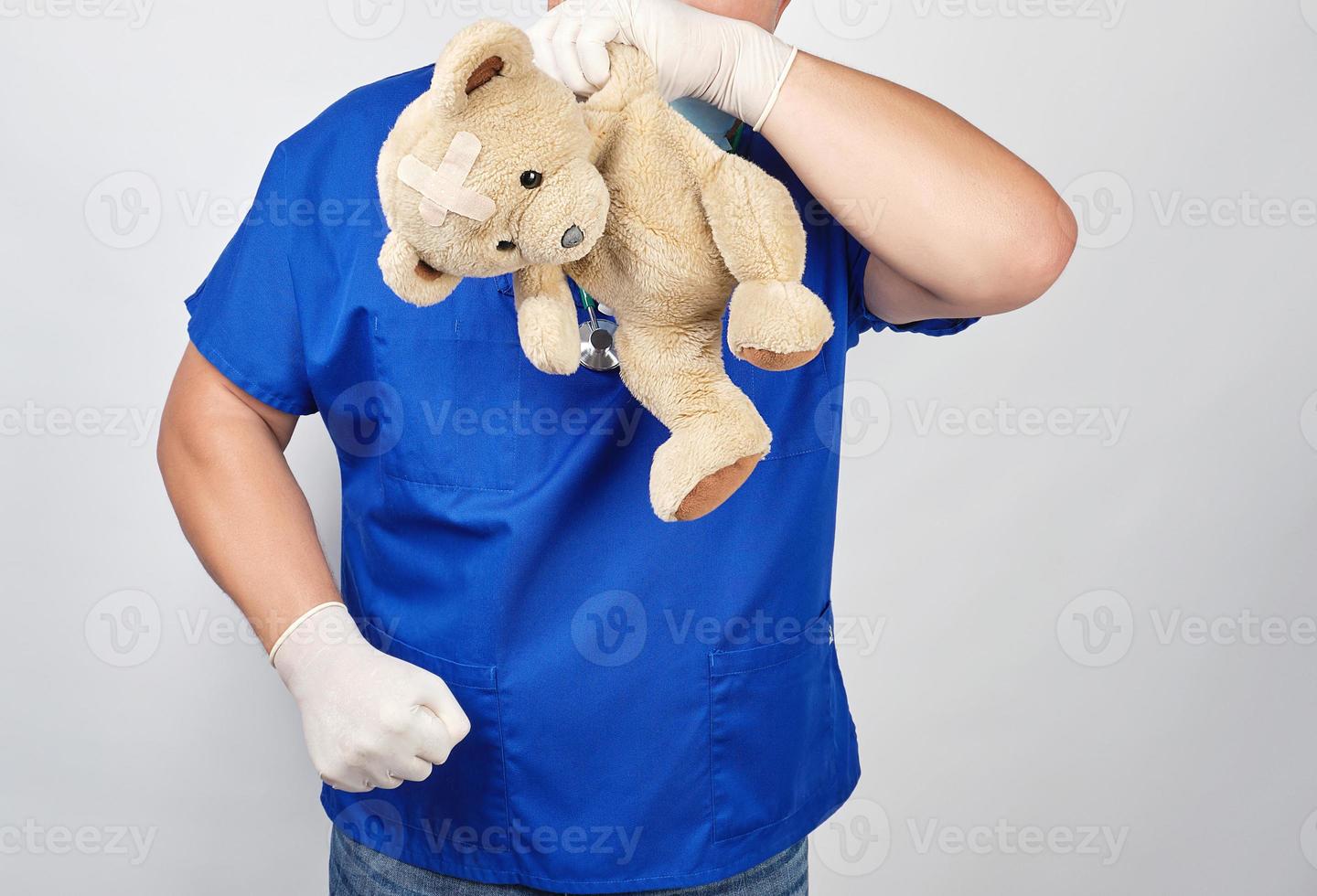 doctor in a blue uniform holding a teddy bear with a plaster near the head in a sign of despair photo