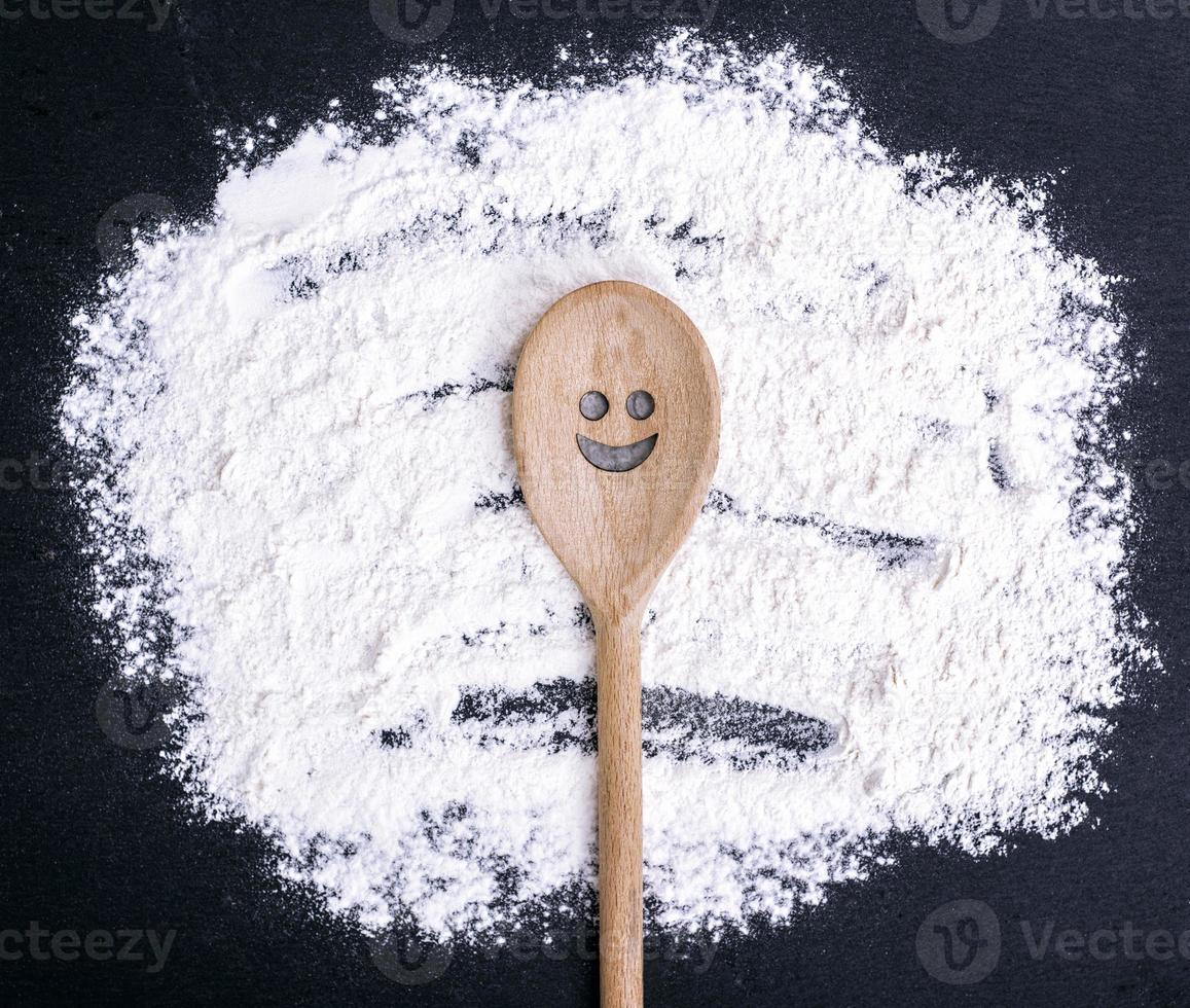 spoon with a carved smiling face lies on scattered flour photo