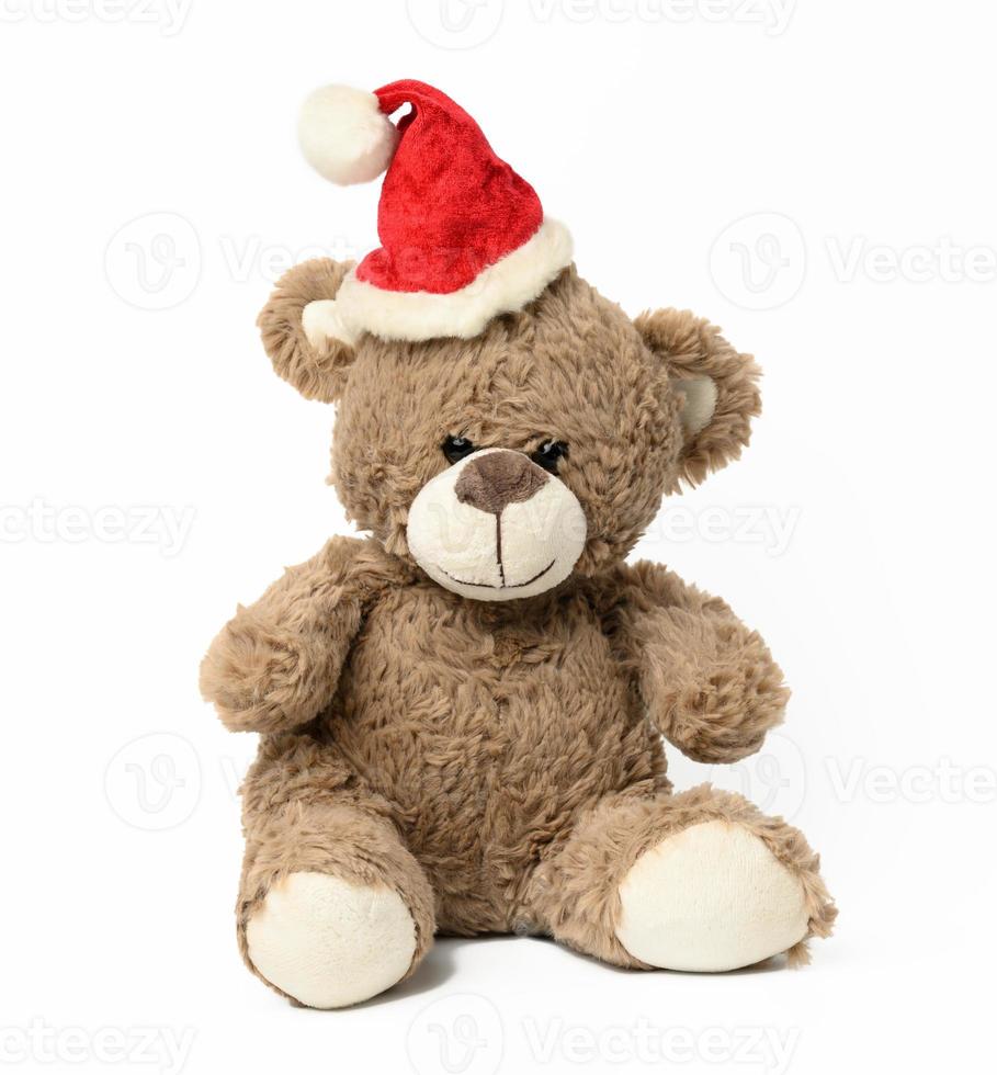 cute brown teddy bear sitting in red christmas cap on white  background photo